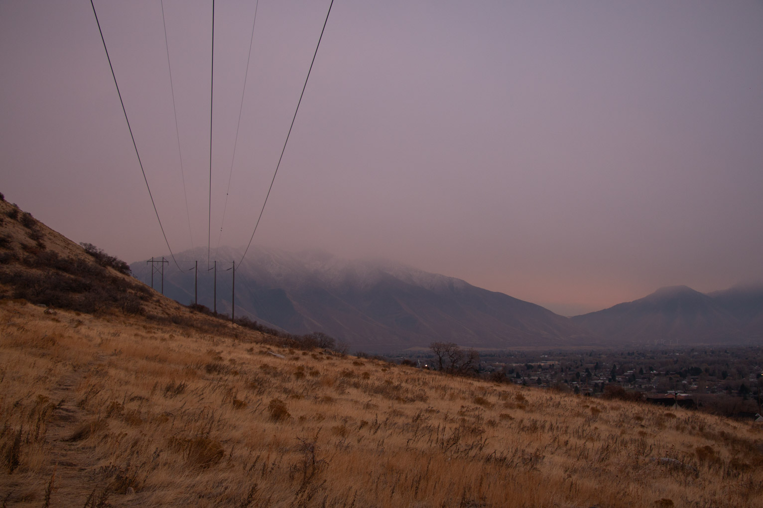 yellow grass mountainside with purple hazy mountain in the distance, powerlines head directly away on the left